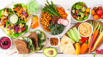 Healthy lunch table scene with nutritious lettuce wraps, Buddha bowl, vegetables, sandwiches, and salad, overhead view over white wood dieta-veg