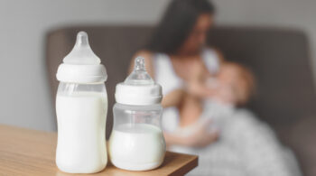 Bottles with breast milk on the background of mother holding in her hands and breastfeeding baby. Maternity and baby care. post-parto