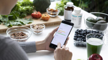 Woman Asian Professional Nutritionist busy working and checking data from a phone with a variety of fruits, nuts, vegetables, and dietary supplements on the table app-peso